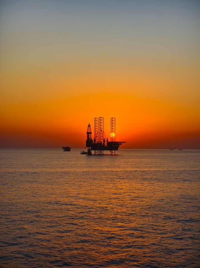 our-mission Silhouette of an oil rig against a vibrant sunset over the ocean, capturing the essence of industrial beauty.